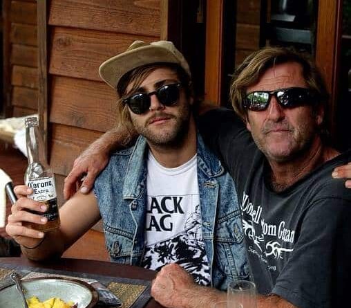 Two men wearing sunglasses are sitting at a table holding hands.